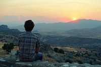 Back view of man sitting on a wall mountain sunset photo.