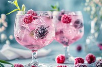 Two nicely decorated cocktail glasses filled with a pink gin tonic beverage with frozen berries berry blackberry raspberry.