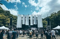 The entrance to an outdoor music festival in Japan with large white hangs a banner structure and below we see many people concert accessories accessory.