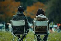 The back of couple sitting on empty white folding chair camping while seeing outdoor concert outdoors furniture walking.