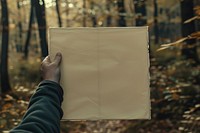 Hand holding blank square paper cover album vinyl record against park outdoors vegetation woodland.