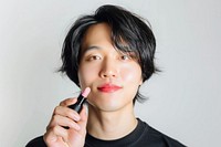 Asian transgender male hand holding pink lipstick with confident pose cosmetics makeup person.