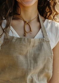 A women wearing light bronw linen fabric apron accessories accessory necklace.