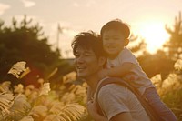 Young asian father carrying son on back outdoors nature photo.