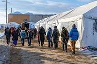 Refugee people lined up in front of medical tents building hat architecture.