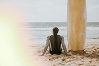 Black man sitting by his surfboard