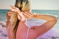 Blonde woman tying a ponytail at the beach back view