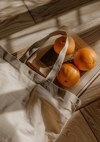 Open tote bag lying on wooden top fill with book and two oranges inside pear produce fruit.