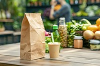 Brown kraft paper bag stands upright at an outdoor table fruit cup beverage.