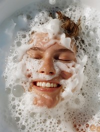 Smiling and relaxing in the bathtub filled with thick white foam bathing washing person.