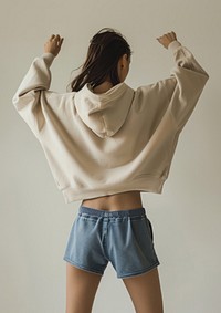 A woman wearing an oversized beige hoodie and blue shorts with a high waistline sweatshirt clothing knitwear.