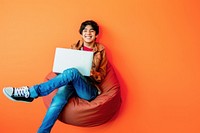 Male teen sitting on bean bag laptop background happy.