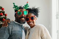 A Happy black couple wearing cute Christmas tree glasses and reindeer antlers glasses celebrating together on a white room background and window on the right side happy christmas christmas tree.