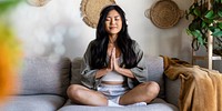 Peaceful Asian woman meditating on sofa