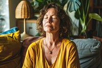 Middle aged woman meditating at home with eyes closed meditation mental accessories.