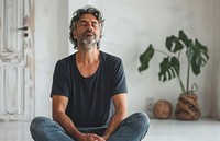 Middle aged man sitting on the floor at home with eyes closed meditation plant mindfulness.