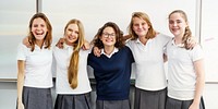 Group of young girls in school uniforms smiling in a classroom. They are wearing white shirts and gray skirts, standing together in front of a whiteboard. Teenage girls in international high school.