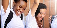 Two young women in white shirts smiling and raising arms. Diverse friendship, and happiness. Celebrating success and friendship with joy and smiles. Diverse young women celebrating success in school.