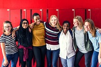 Diverse group of girls, including different ethnicities, standing together at lockers and smiling. Girls front of red lockers, women showing unity and friendship. Diverse teenage students at school.