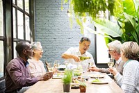 Diverse group of elderly friends, Asian man, Asian woman, African American man, enjoying a meal together. Elderly friends sharing a meal. Diverse retired friends having wine for lunch at a restaurant.