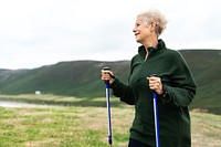 Elderly woman hiking with poles, enjoying nature. Elderly woman hiking in countryside. Active elderly woman, hiking with determination and joy. Senior woman walking with sticks, wellness at older age.