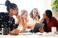 A diverse group of four women collaborate brainstorm around a table, sharing ideas and brainstorm with a tablet, showcasing teamwork and creativity. Diverse women meeting and brainstorm for new ideas