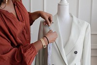 A black woman fashion designer measuring a white blazer on a dress form. This fashion designer focuses on precision in tailoring, showcasing her skills in custom clothing design.