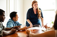 A diverse group in a meeting room. A curby woman leads the meeting. The group, including an Asian man, listens attentively. Meeting room with diverse participants. Business team meeting in boardroom.