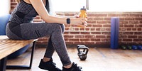 Fit woman in workout clothes with water bottle in a gym after exercise. Woman drink water after workout and exercise at fitness gym. Woman sitting with kettlebell and workout equiptment at fitness