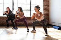 Diverse women exercising in a gym. Women in workout clothes doing squats. Fitness focused women in a gym setting. Women in a gym, training in a gym together. 