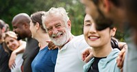 Elderly man and diverse people hugging each other. Diverse group of women and men embrace each other at park. Unity and teamwork. Backside of old man and friends standing in row huddle on green grass.