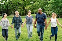 Diverse group of friends hold hands at park. Diverse group of men and women standing together hold hands at park. Diverse group of friends, men and women, standing in row hold hands on grass.