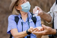 Senior woman wearing a mask receives hand sanitizer from a man. The woman, in a mask, enjoying outdoors. Senior woman using hand sanitizer. Senior couple enjoying outdoors adventure