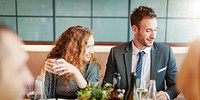 A man and woman at a restaurant table, smiling and enjoying drinks. They are dressed in business attire, with wine glasses and a modern setting in the background. Business man and woman at lunch.