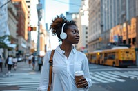 An african american woman in white shirt walking with a coffee and wireless headphone city headphones adult.