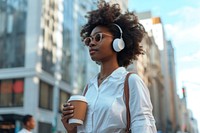 An african american woman in white shirt walking with a coffee and wireless headphone headphones glasses city.