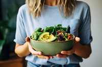 Woman in t-shirt and jeans standing and holding vegan bowl or salad bowl in kitchen adult food midsection. 