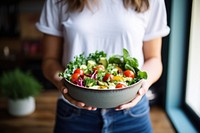 Woman in t-shirt and jeans standing and holding vegan bowl or salad bowl in kitchen adult plant food. AI generated Image by rawpixel.