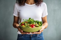 Woman in t-shirt and jeans standing and holding vegan superbowl or salad bowl food midsection vegetable. AI generated Image by rawpixel.