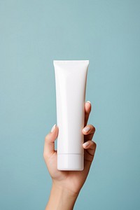 Hand holding tiny squeeze bottle plastic tube container of cream toothpaste cosmetics sunscreen.