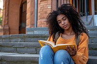 African American teenage reading sitting book.