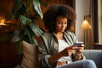 Young Black woman managing online banking with smartphone sitting on the sofa adult head portability.