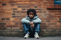 Black boy sitting on the street worried brick wall.