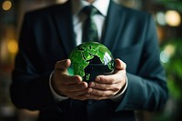 A man in a suit holding a small green globe sphere adult accessories.