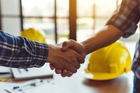 Two architects people shaking hands in front of yellow hard hats on desk handshake hardhat helmet.