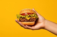 Hamburger on hand holding yellow food.