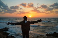 Young Palestinian man arms outstretched sea outdoors horizon.