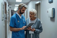 A man in blue hospital doctor costume showing his tablet to an old woman in gray sweater computer adult nurse. AI generated Image by rawpixel.