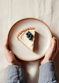 A person holding piece of blueberry pie on plate cheesecake dessert food.