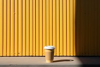 A paper coffee cup and business card onto a barricaded fence yellow wall architecture.